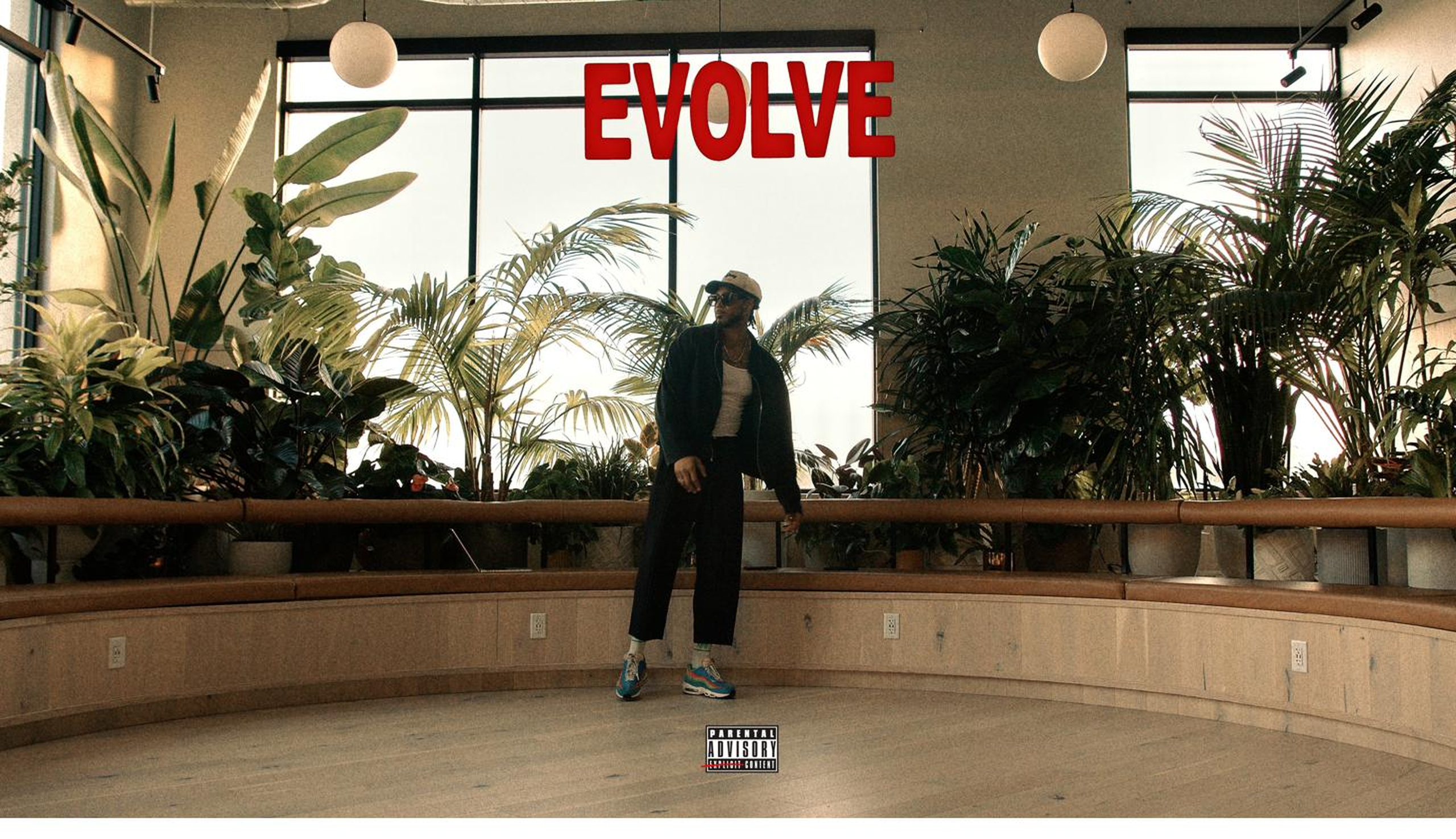 EVOLVE album cover - Kyle Prater in the plant room beneath the red EVOLVE marquee